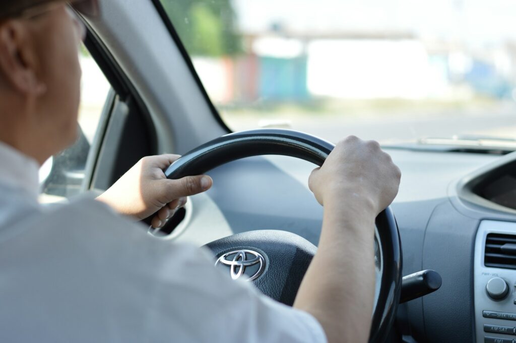 Driver hand resting on steering wheel of car interior