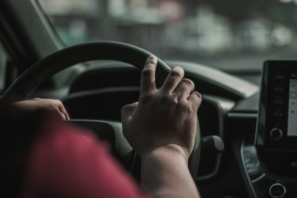 A person driving a car with a hand on the steering wheel
