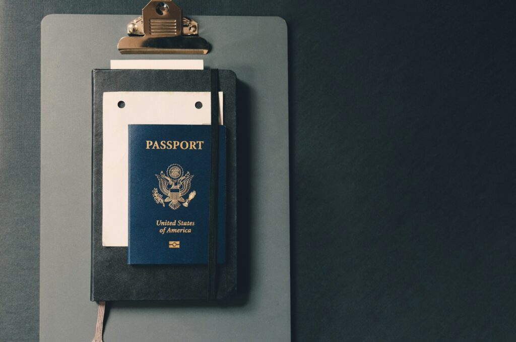 A passport resting on a brown clipboard with a pen