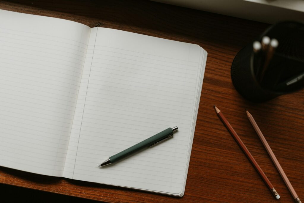 Open notebook with pen and pencils on a clean wooden study desk