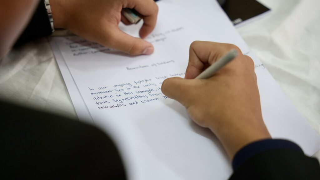 A person writing answers on a printed test paper with a pen