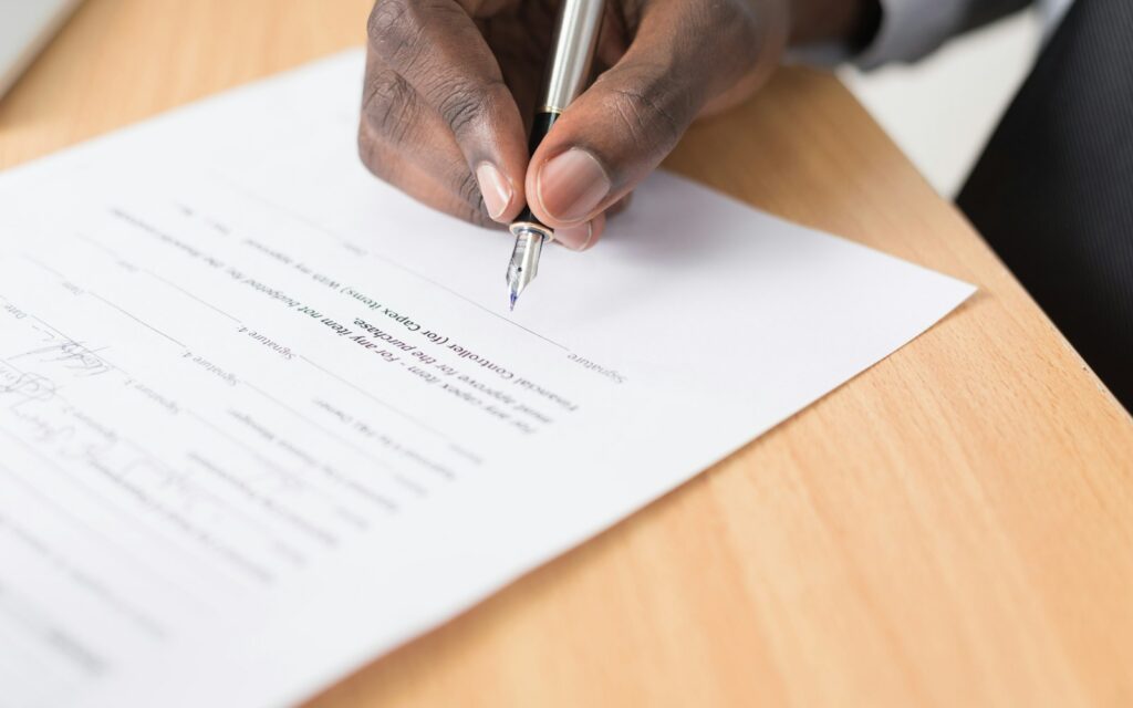 A person writing on a paper form with a pen at a desk