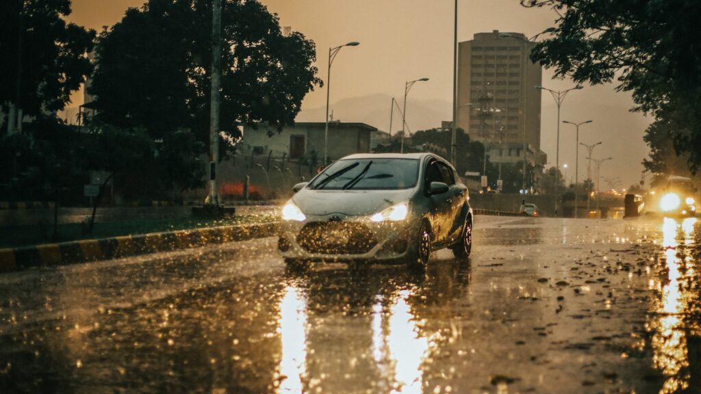 A car driving down a rain-soaked street at dusk