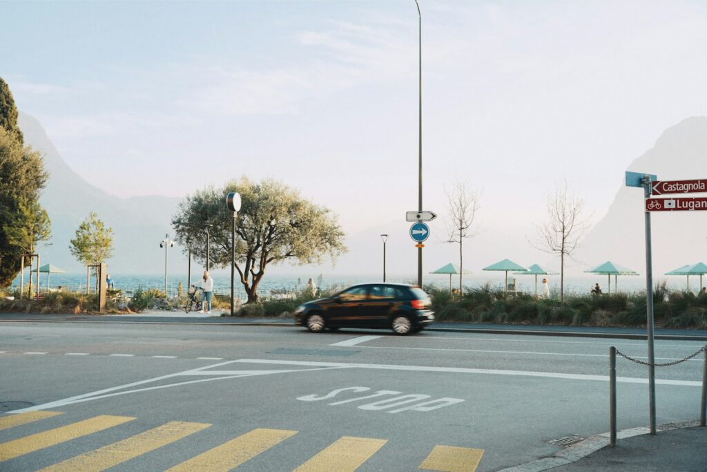 A black car stopping at a stop sign at a rural intersection with a lake and mountains
