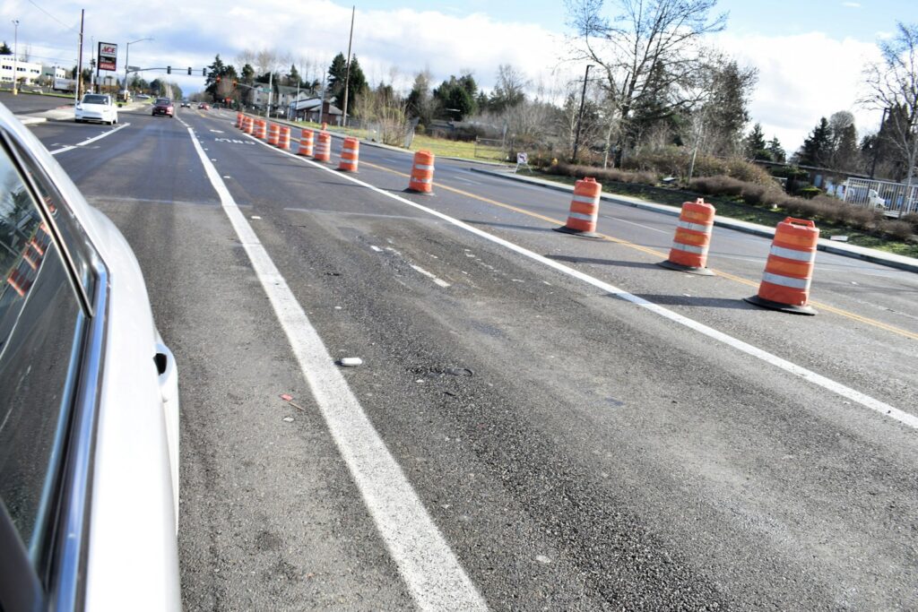 A car drives past orange traffic cones marking a road work zone