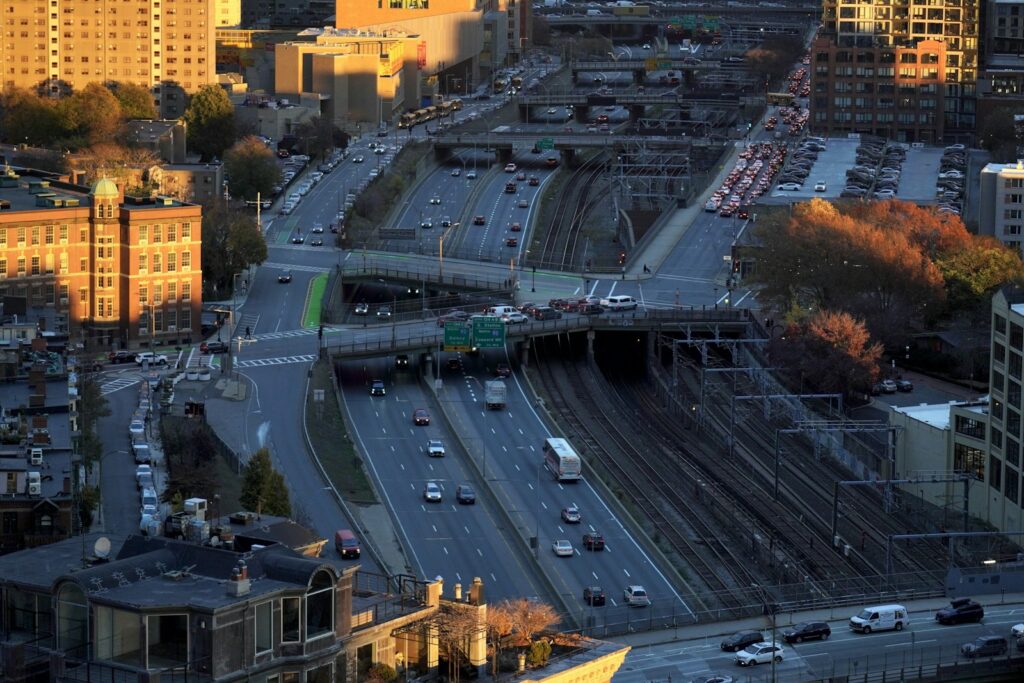 Aerial view of traffic on Interstate 90 and train tracks beside brick buildings in Boston at sunset