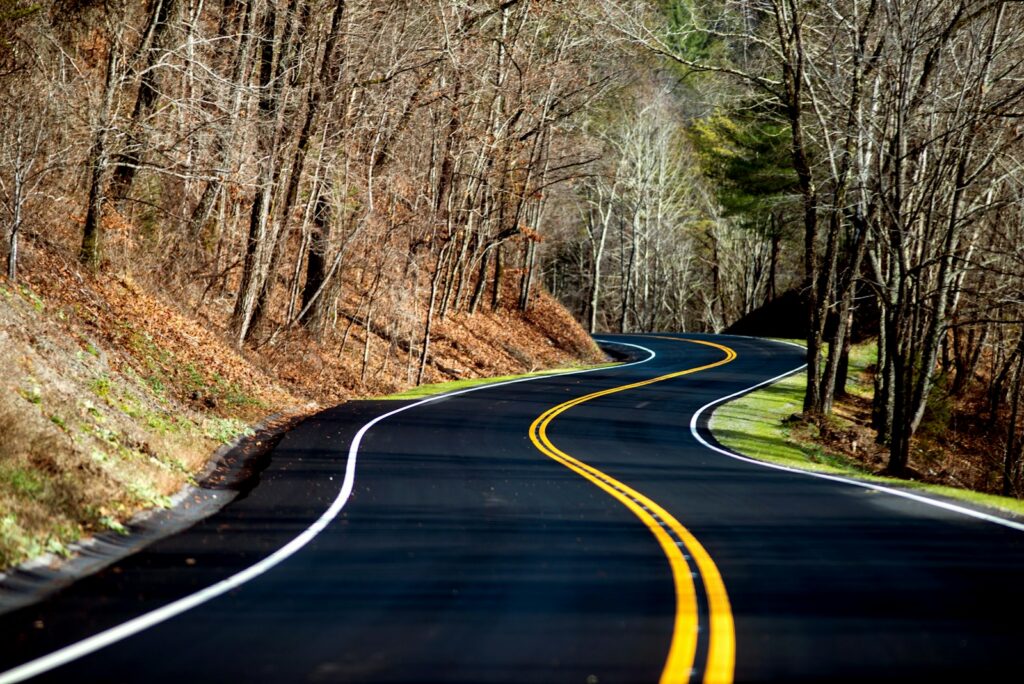 A two-lane road curving out of sight through open country, the kind of blind curve where a no-passing zone begins