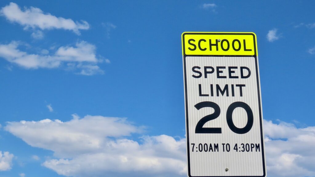 A US school zone speed limit sign reading SCHOOL SPEED LIMIT 20, 7:00AM to 4:30PM against a blue sky