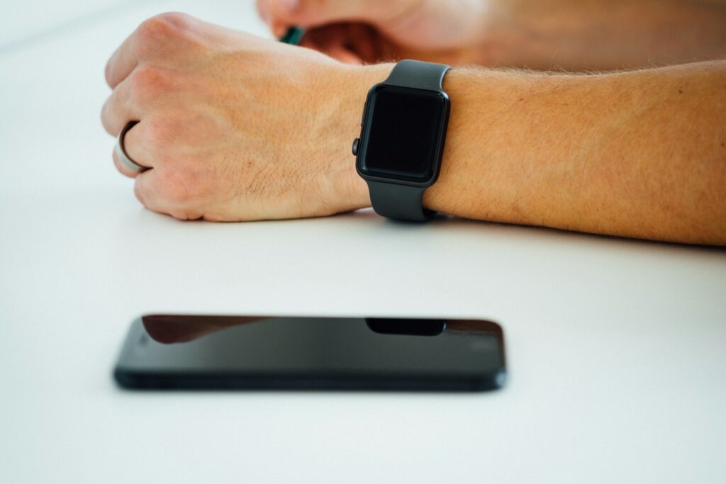 A black smartphone lying beside a hand wearing a black smartwatch