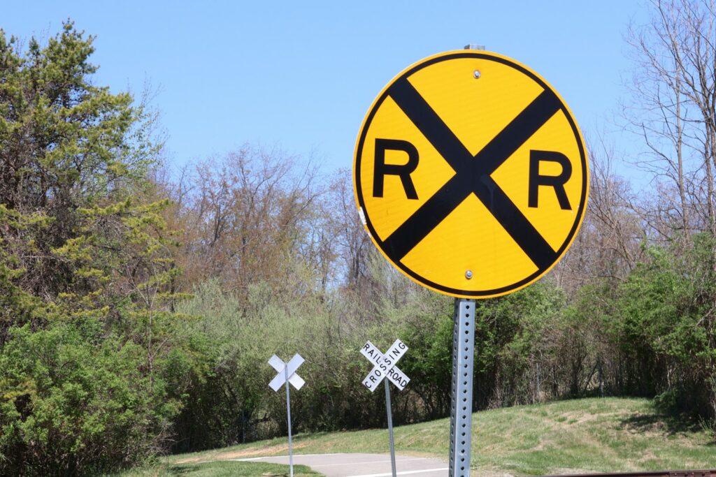 Round yellow railroad advance warning sign beside a rural road with a white crossbuck sign standing behind it