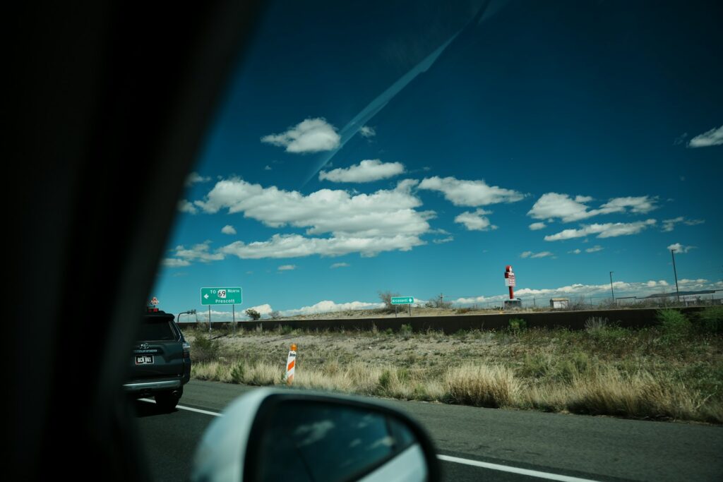 Green highway guide signs and an orange channelizer drum seen from a car on a US interstate