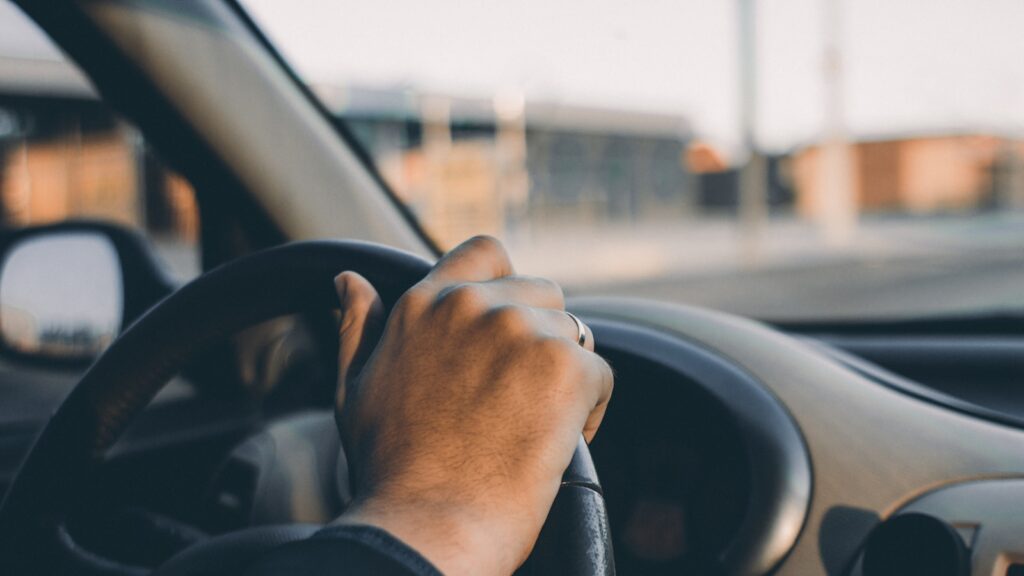 Person in a black long sleeve shirt driving a car with both hands on the steering wheel