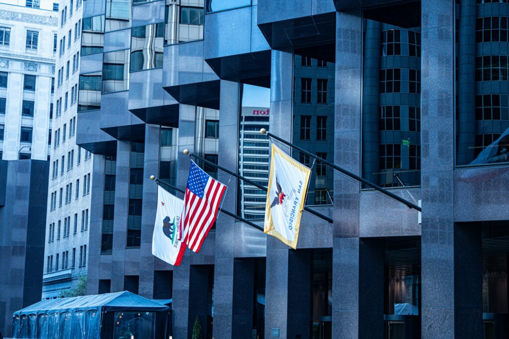 United States, California state and San Francisco city flags on poles outside a downtown office building