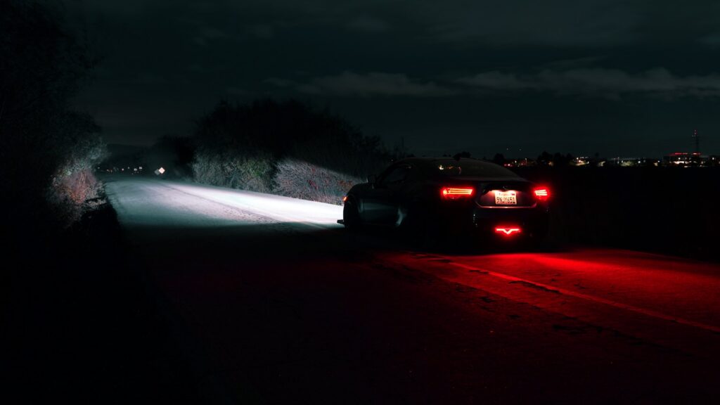 A car on an unlit road at night, its headlights casting light on the pavement ahead