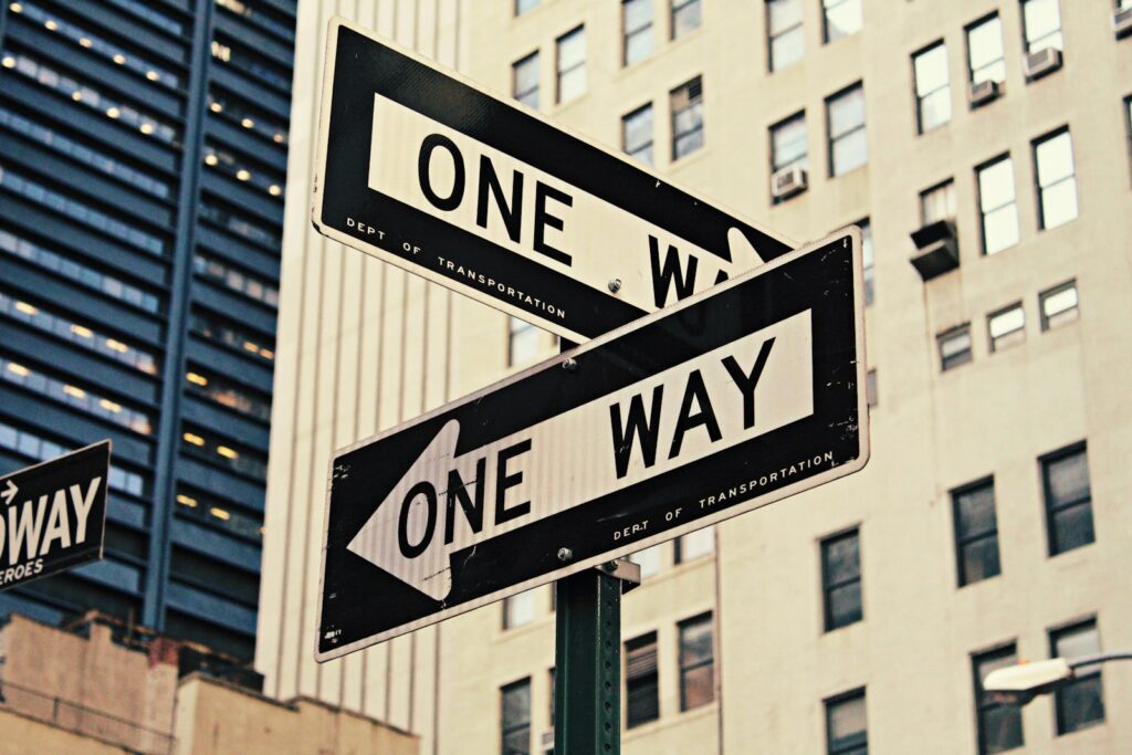 White and black ONE WAY street signs mounted on a pole above a city street