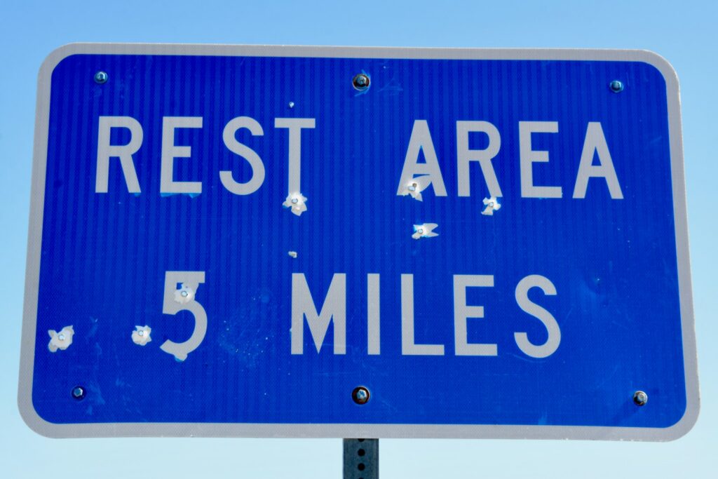 Blue REST AREA 5 MILES highway sign with white lettering against a clear sky