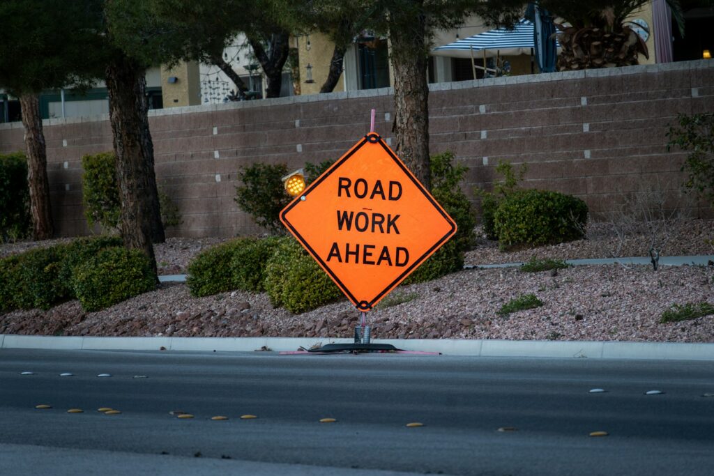 Orange diamond ROAD WORK AHEAD sign standing at the edge of a street with traffic behind it